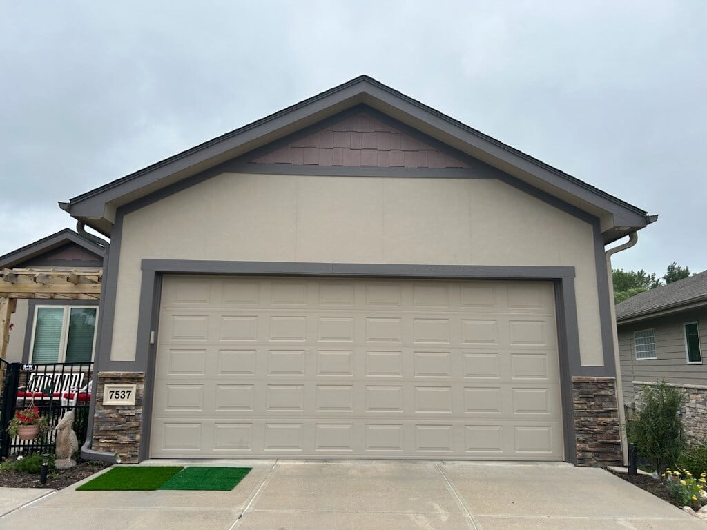 Beige colored garage door with a darker gray painted trim around it with maroon detailing at the peak of the garage door.