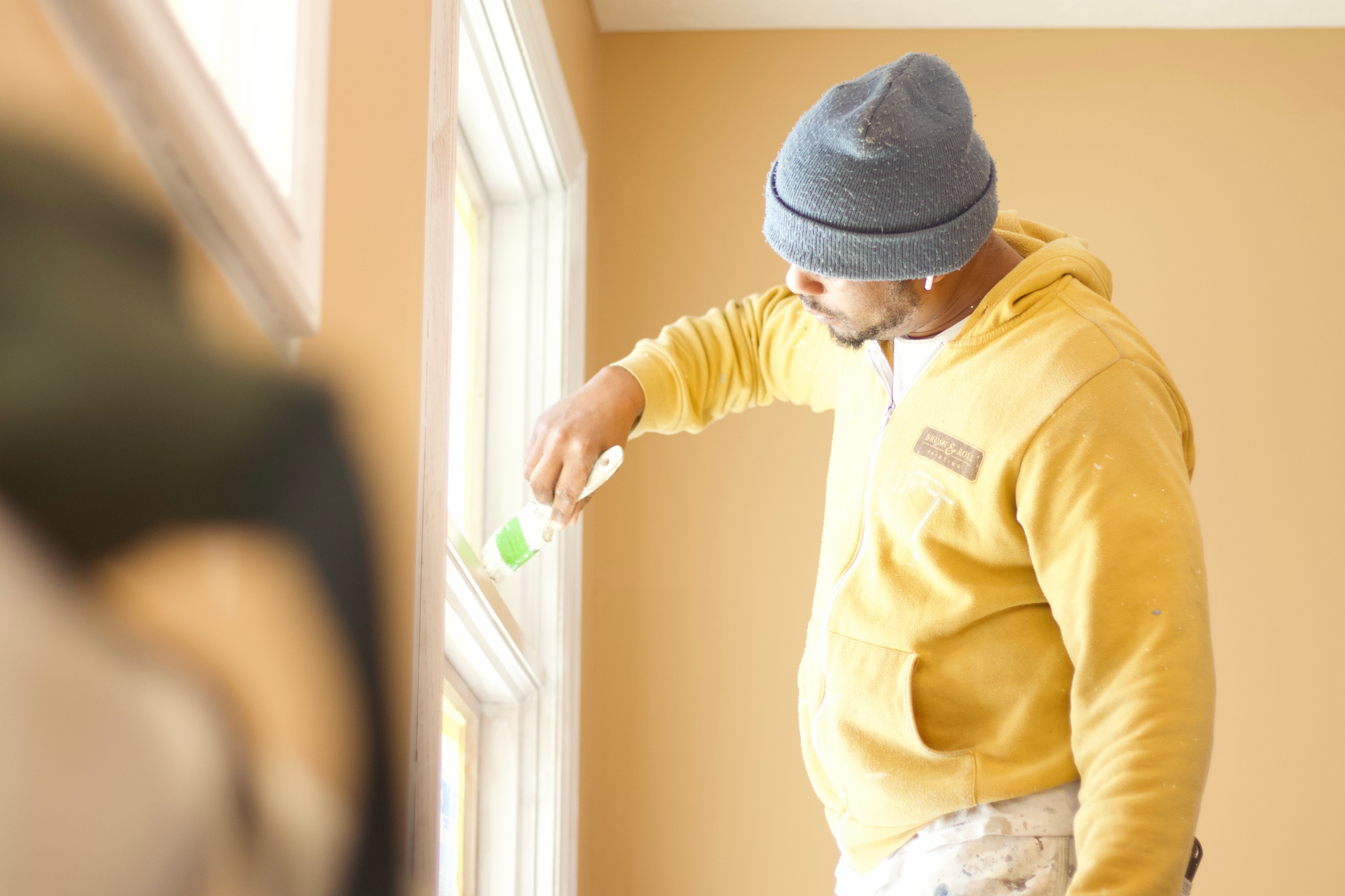 Painter brushing white paint onto window trim inside of a home in Omaha, NE.