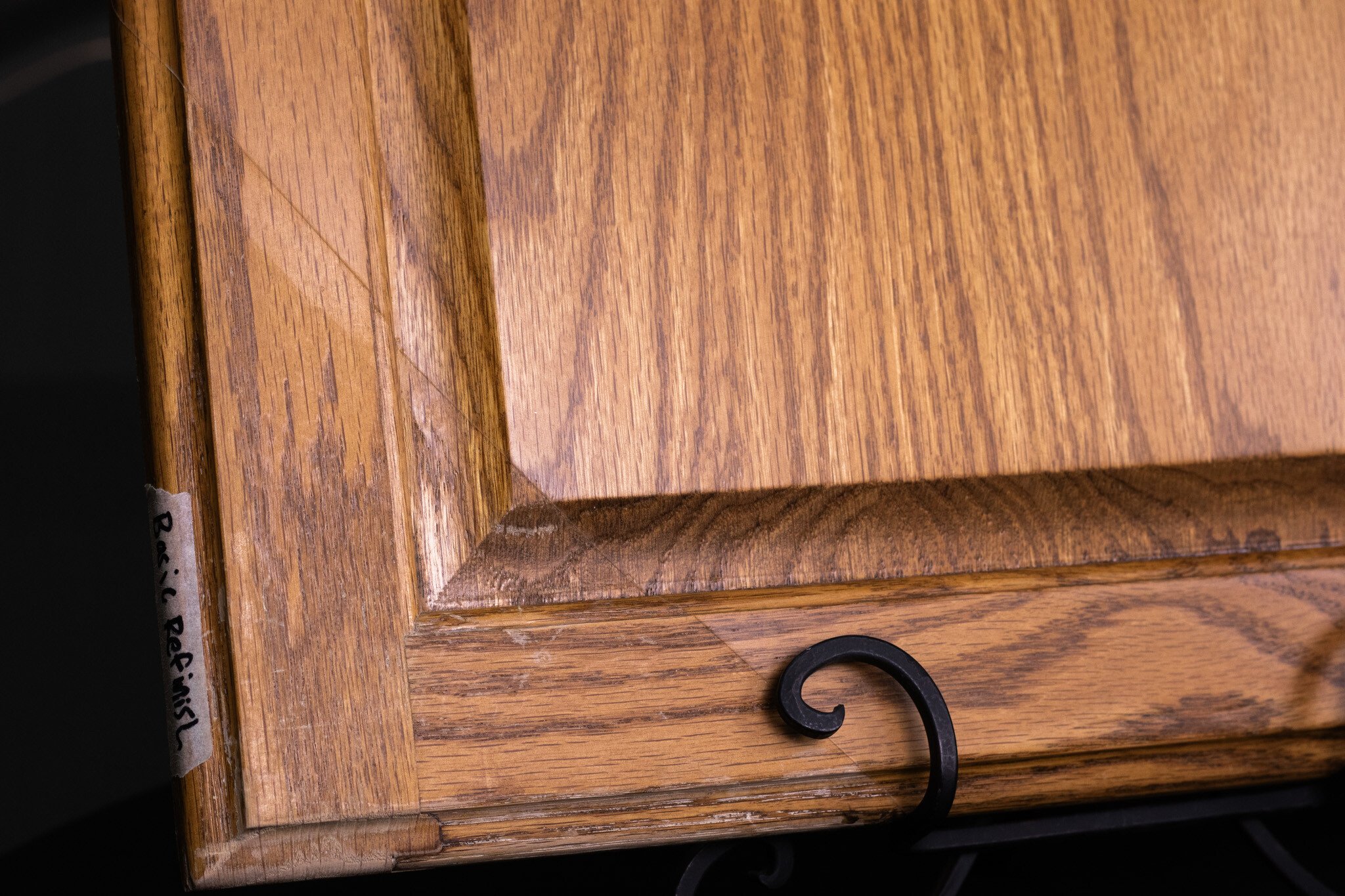 Golden oak cabinet door with a basic refinish on entire door except for a corner. Corner of the oak door shows a duller, imperfect finish.