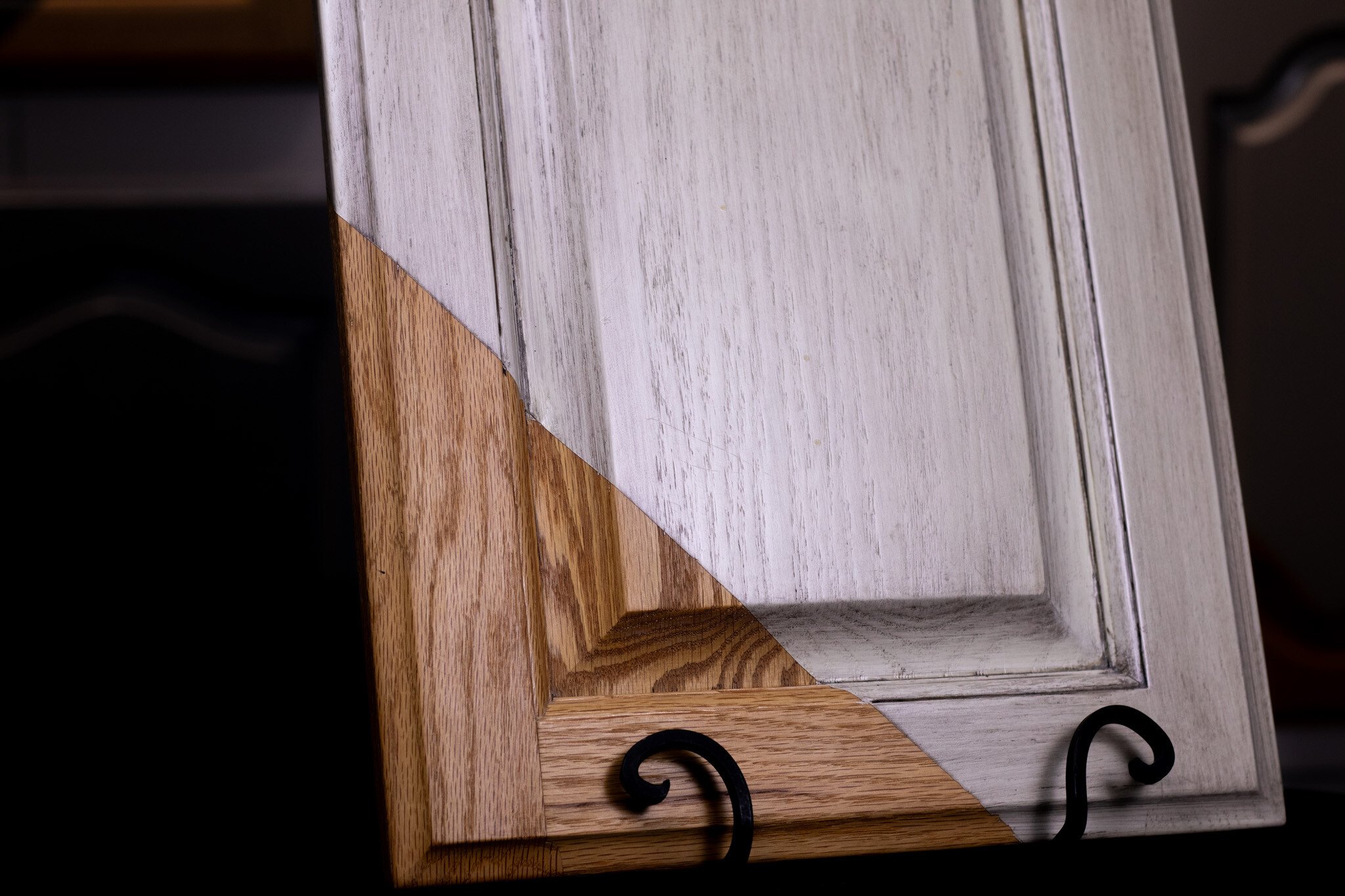 Distressed white cabinet door with grain showing through the paint. Corner of the cabinet door is untouched by paint and is natural wood.