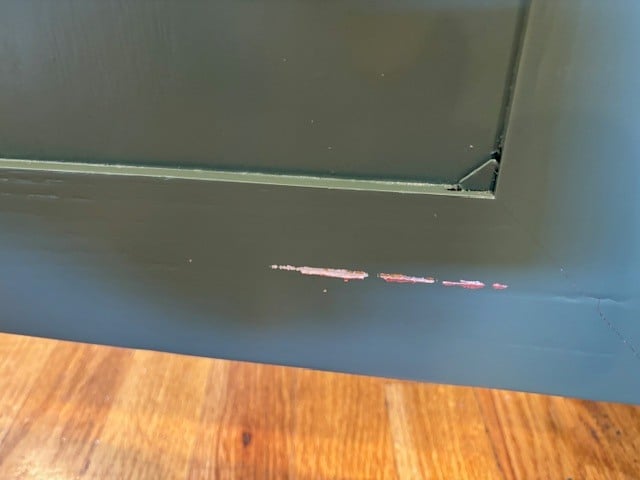 Inside of dark green painted cabinet door scraped by a trash can holder.