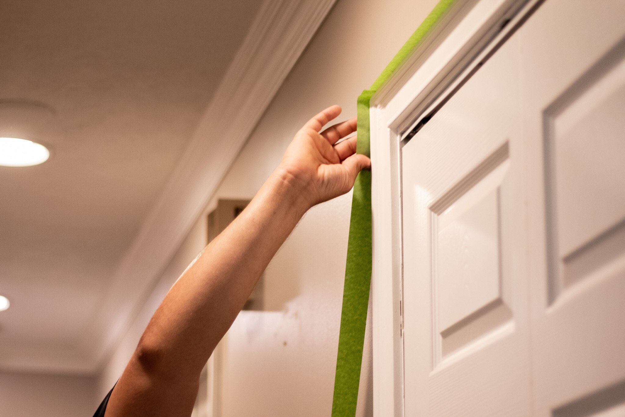 Painter applying green tape to the outside of a interior door trim painted white before painting the walls.