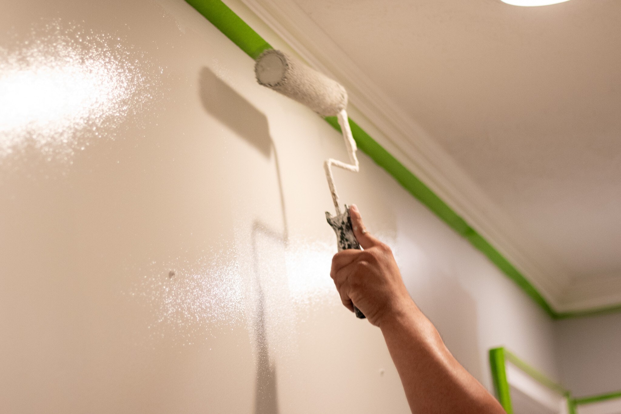 Painter rolling off white paint on a wall with a paint roller.