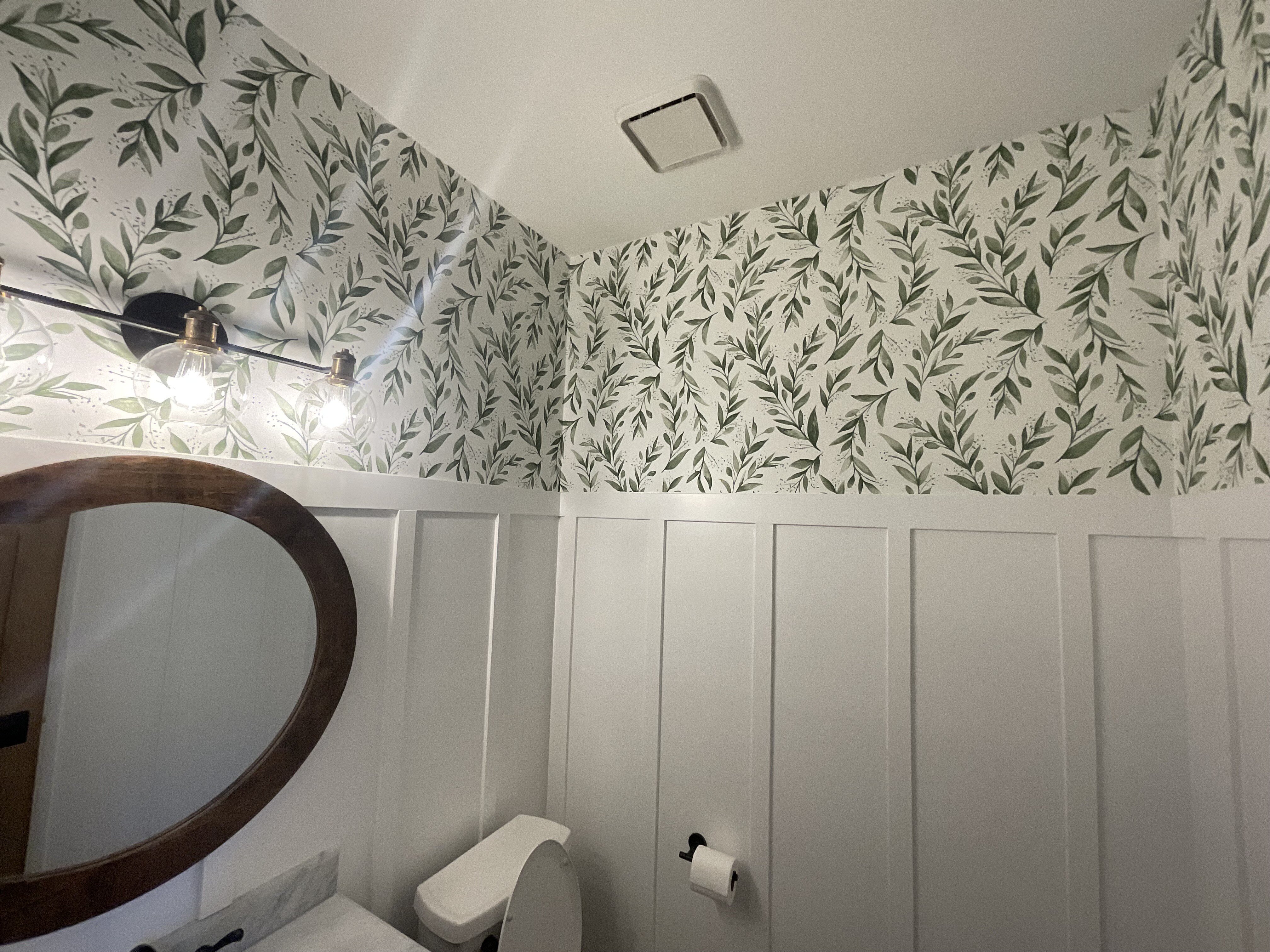 Bathroom with wallpaper on upper half and board and batten on lower half painted white.
