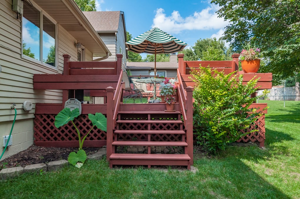 Deck in a persons backyard stained a deep red tone with bushed around the deck.