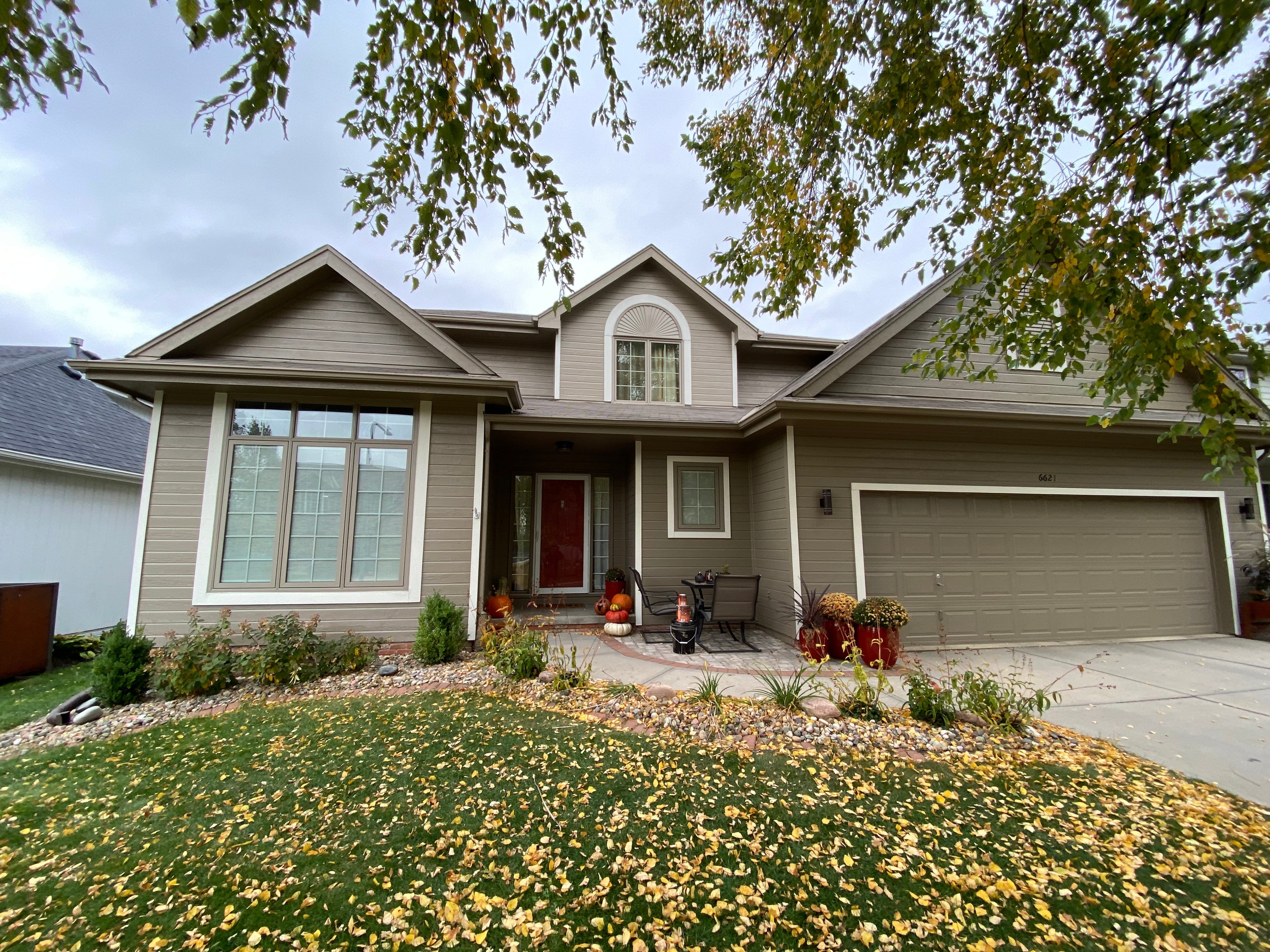 Light brown, two-story home exterior with fall leaves on grass and pumpkins on front porch.