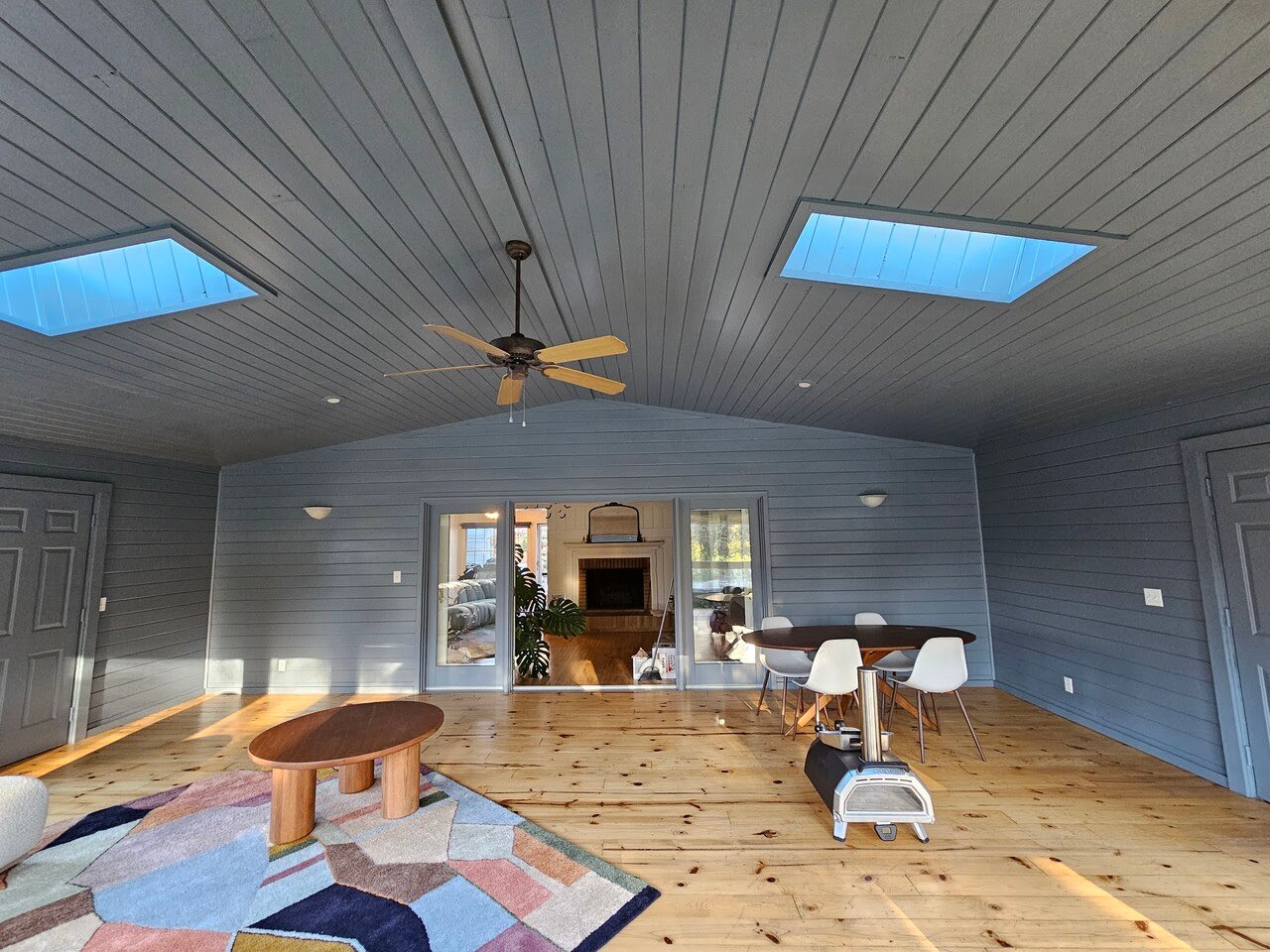 Interior sunroom with ceiling and walls painted the same, dark off black color, with warm wood floors and a large grey couch.