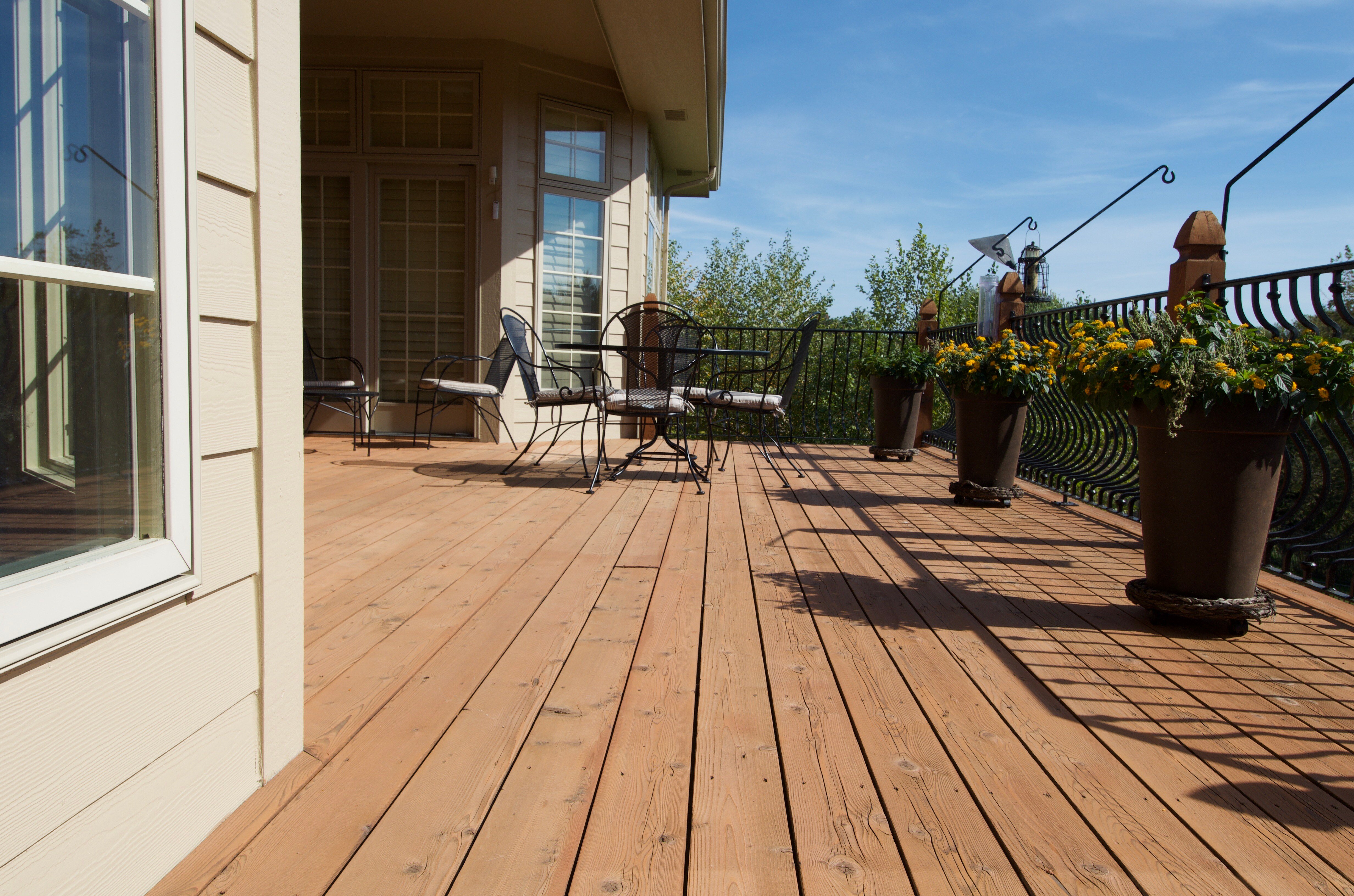 Deck freshly stained with a warm brown wood deck stain, with outdoor chairs and flowers in pots sitting on the deck.