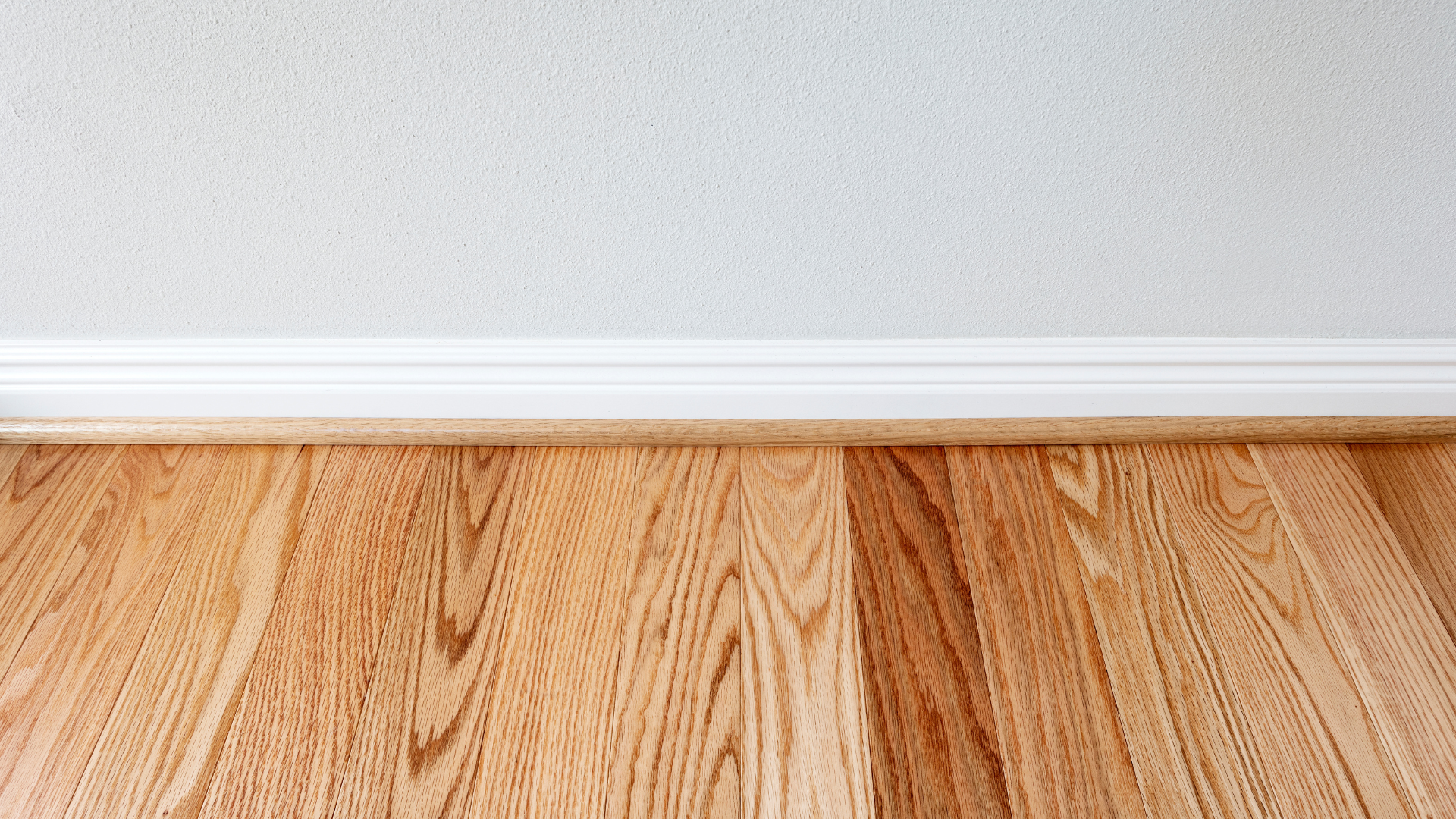 Trim in home in process of being painted white from oak wood with warm oak floors and a grey painted wall.