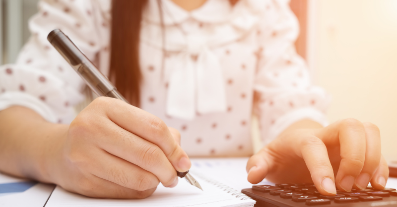 woman writing with pencil and using calculator