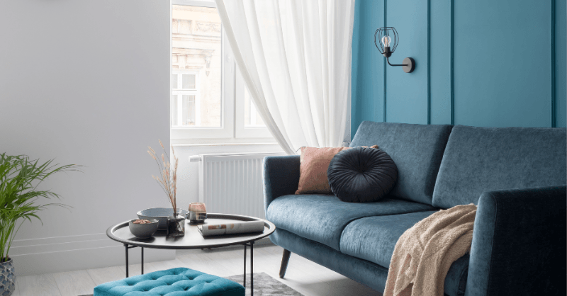 Blue nova color of the year painted on accent wall with gray couch in living room.