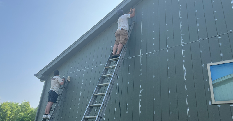 Two painters on ladders caulking the exterior of a home before painting.