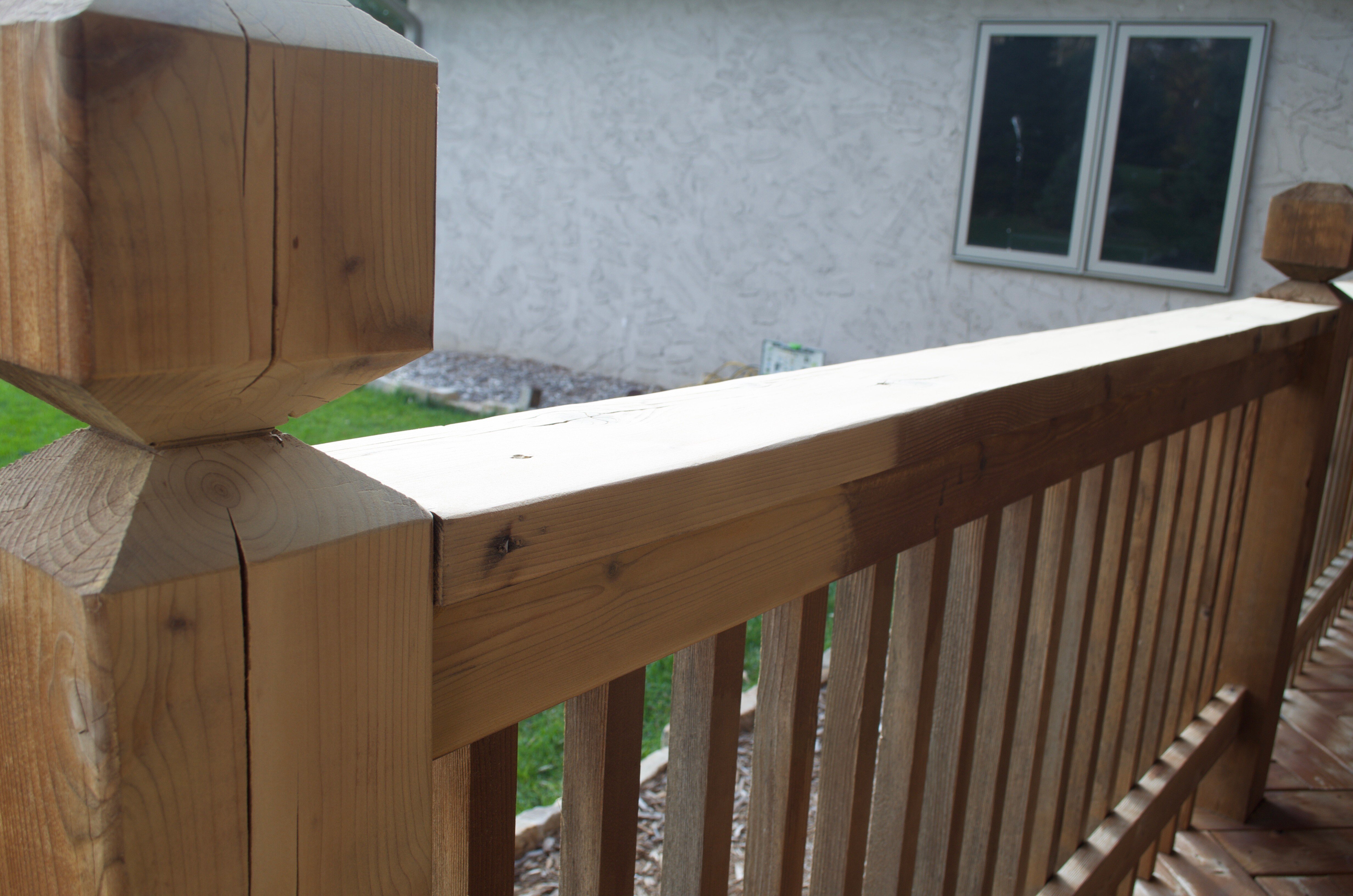 Deck with a railing half stained with a dark brown shade and the other raw natural wood.