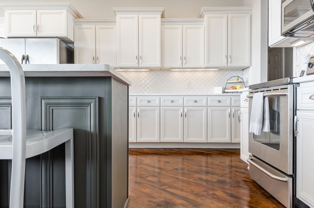 Kitchen with white upper and lower cabinets and a sage green painted cabinet island. The kitchen was renovated and has wood flooring and stainless steel appliances.