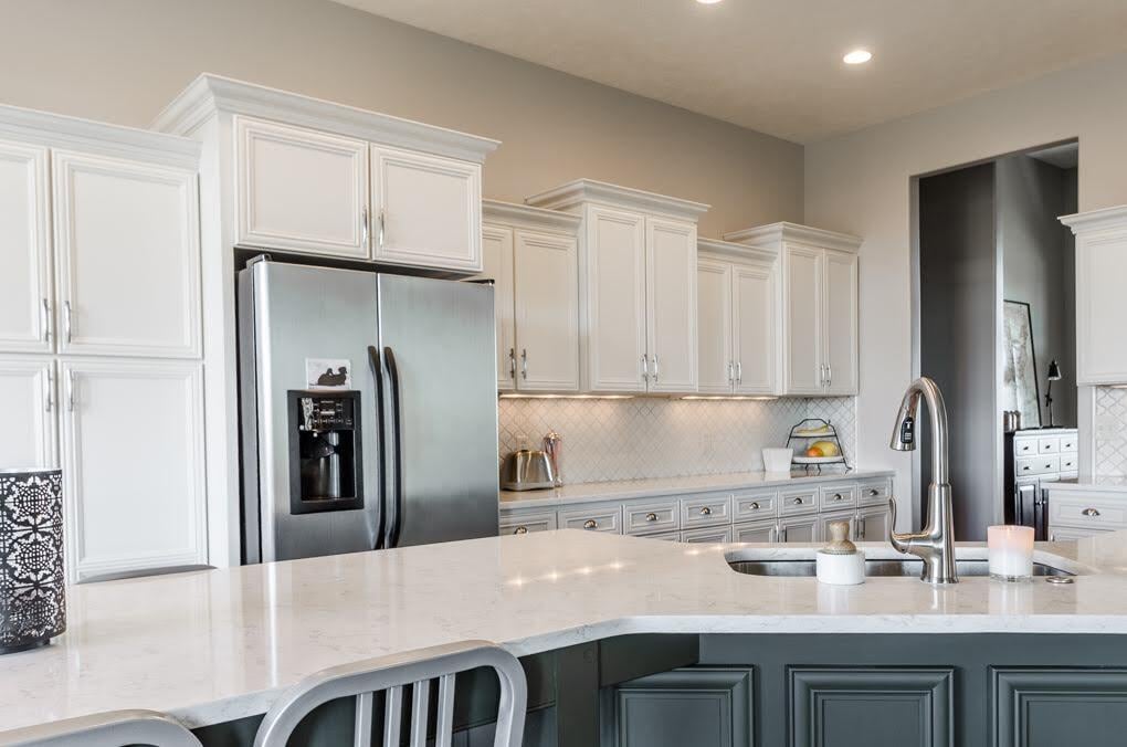 White painted kitchen cabinets with beige walls and a dark sage green kitchen island and white countertops.