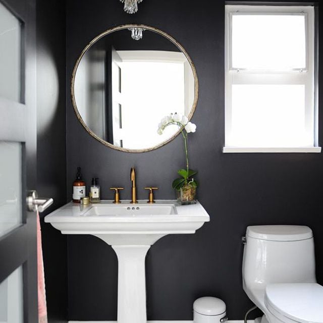 Small bathroom with black walls and interior door and white window trim, toilet, and sink.