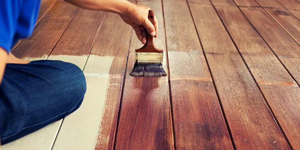 Man applying stain with a brush to a wooden deck.