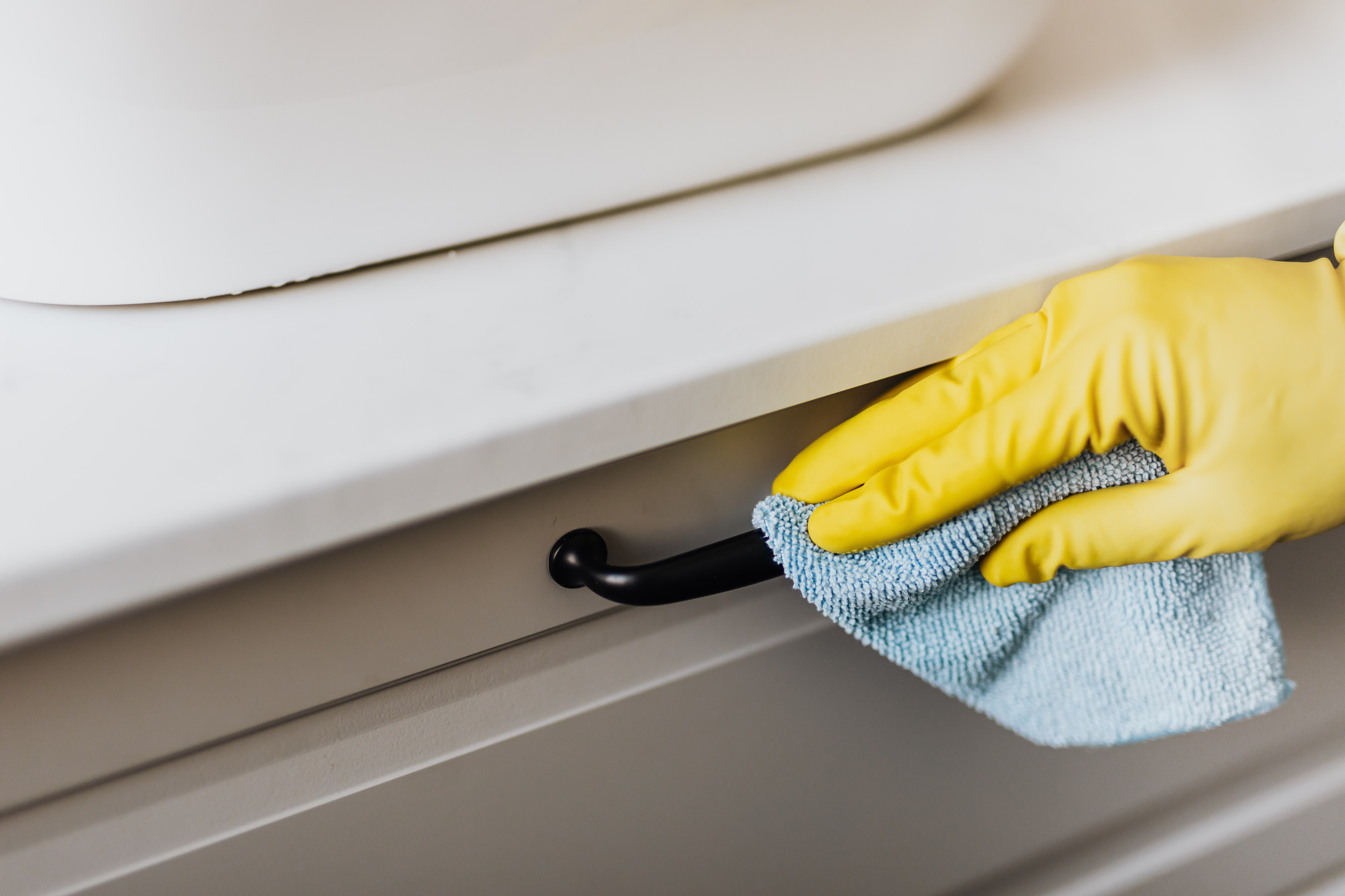 Person wiping kitchen cabinet drawer handles with a rag.